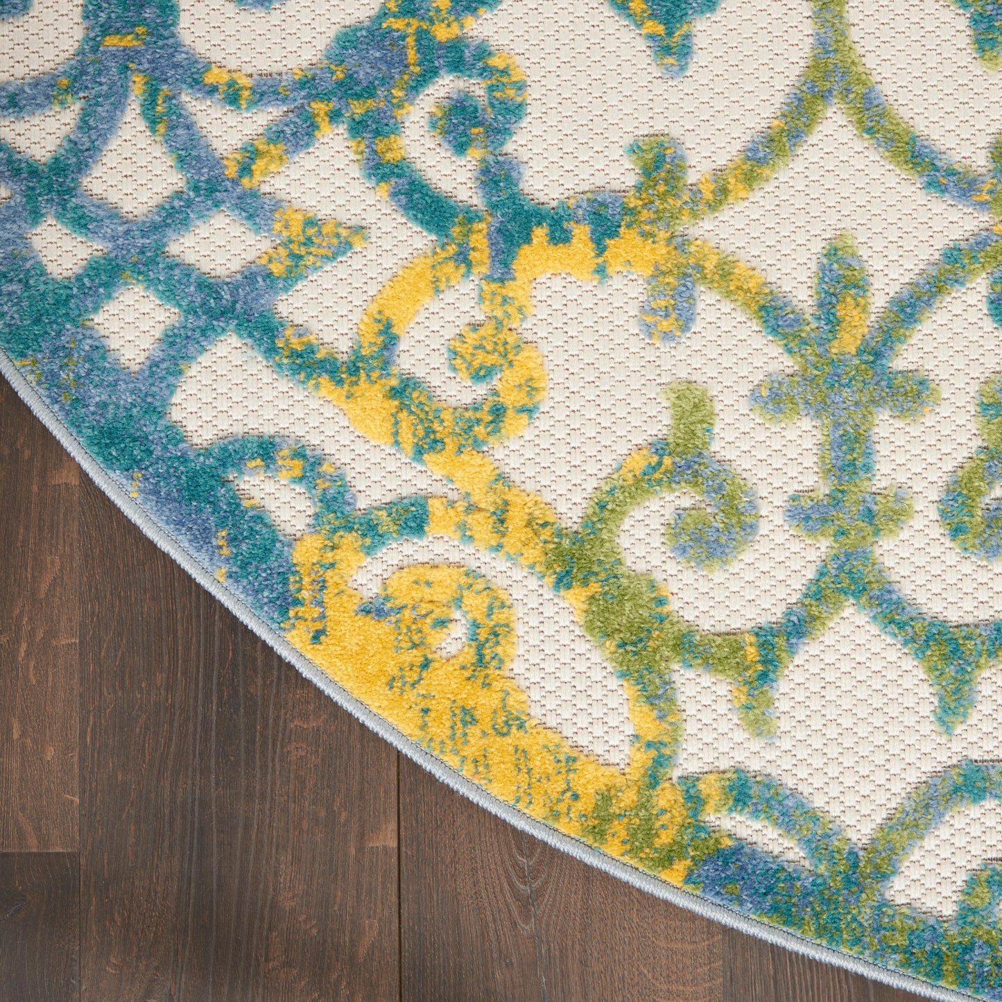 Round rug with blue, teal & yellow ornate pattern on cream background; textured weave, curved edge on dark wood floor.