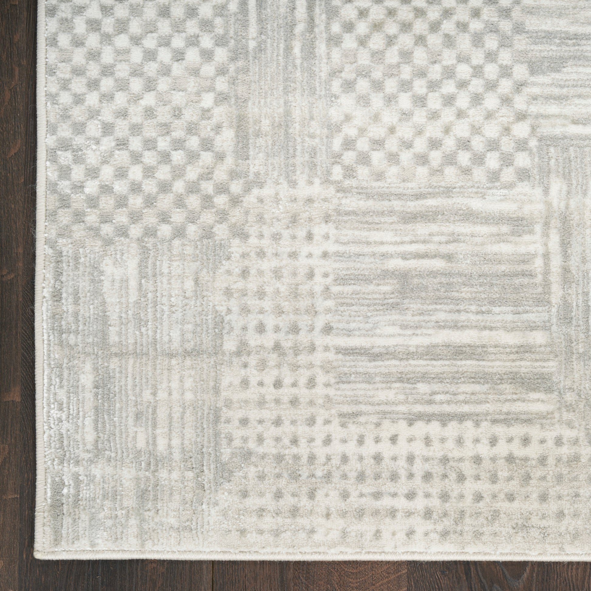Rectangular grey and cream patchwork rug with geometric patterns on dark wood floor.