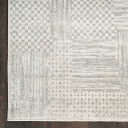 Rectangular grey and cream patchwork rug with geometric patterns on dark wood floor.