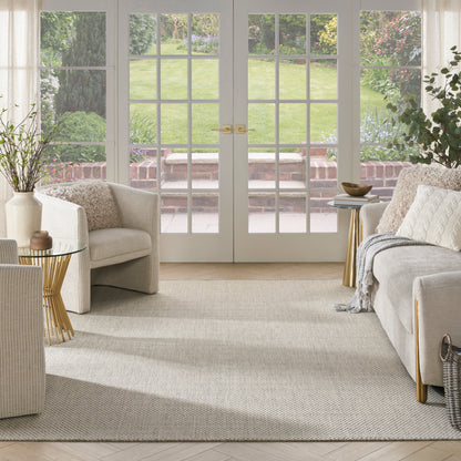 Bright neutral living room with cream sofa, beige armchairs, gold-legged side tables, light rug, and French doors to garden.