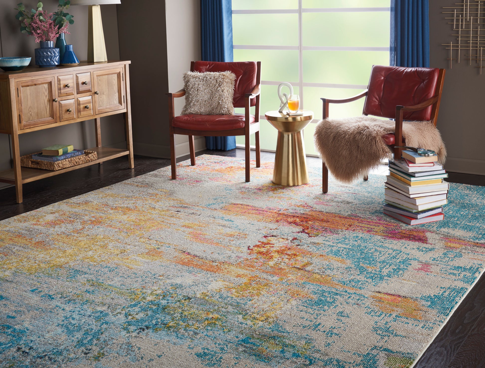 Cozy living room with a colorful abstract rug, two red chairs with fur throws, gold side table, books, and a wooden console.