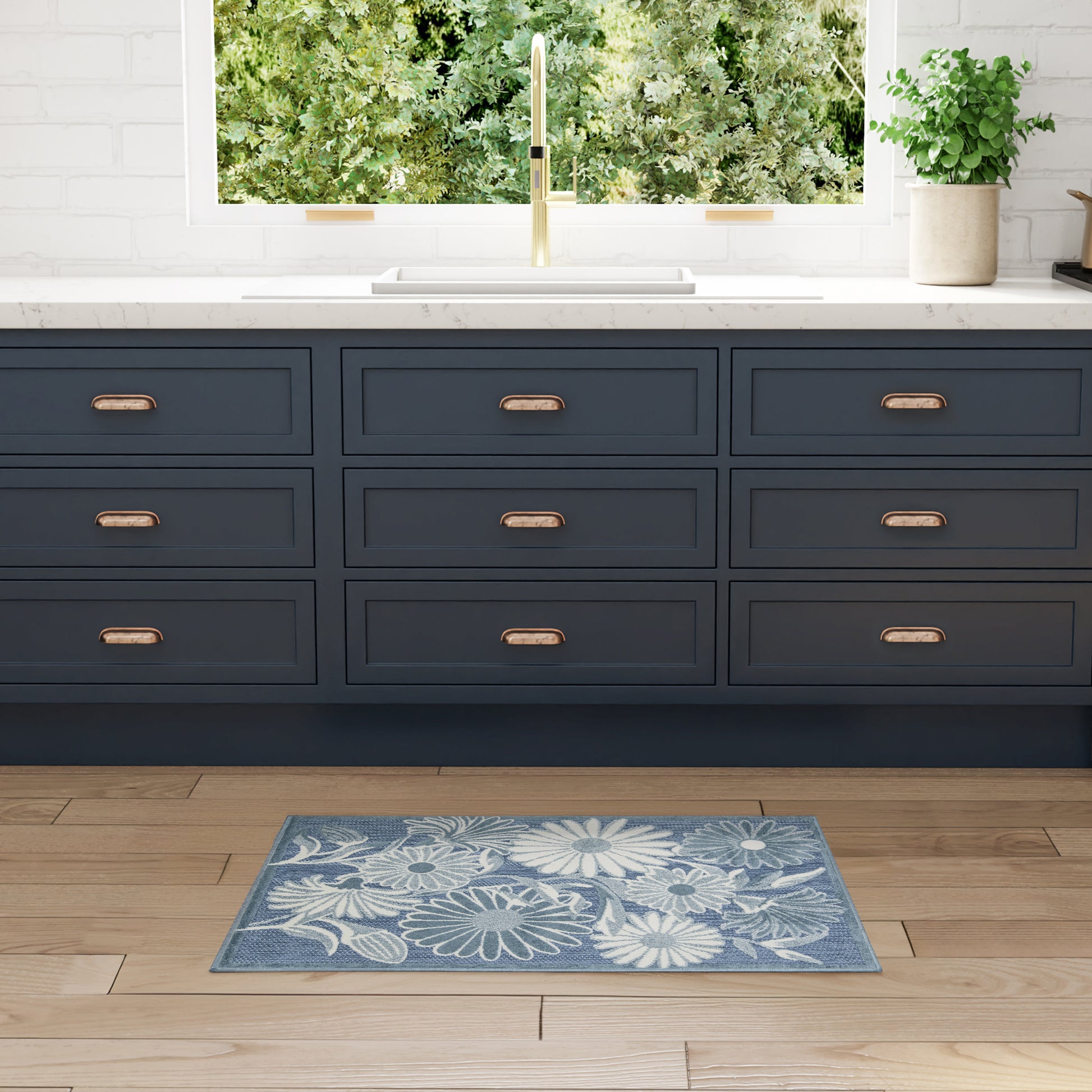 Blue floral outdoor rug on wood floor with greenery in view.
