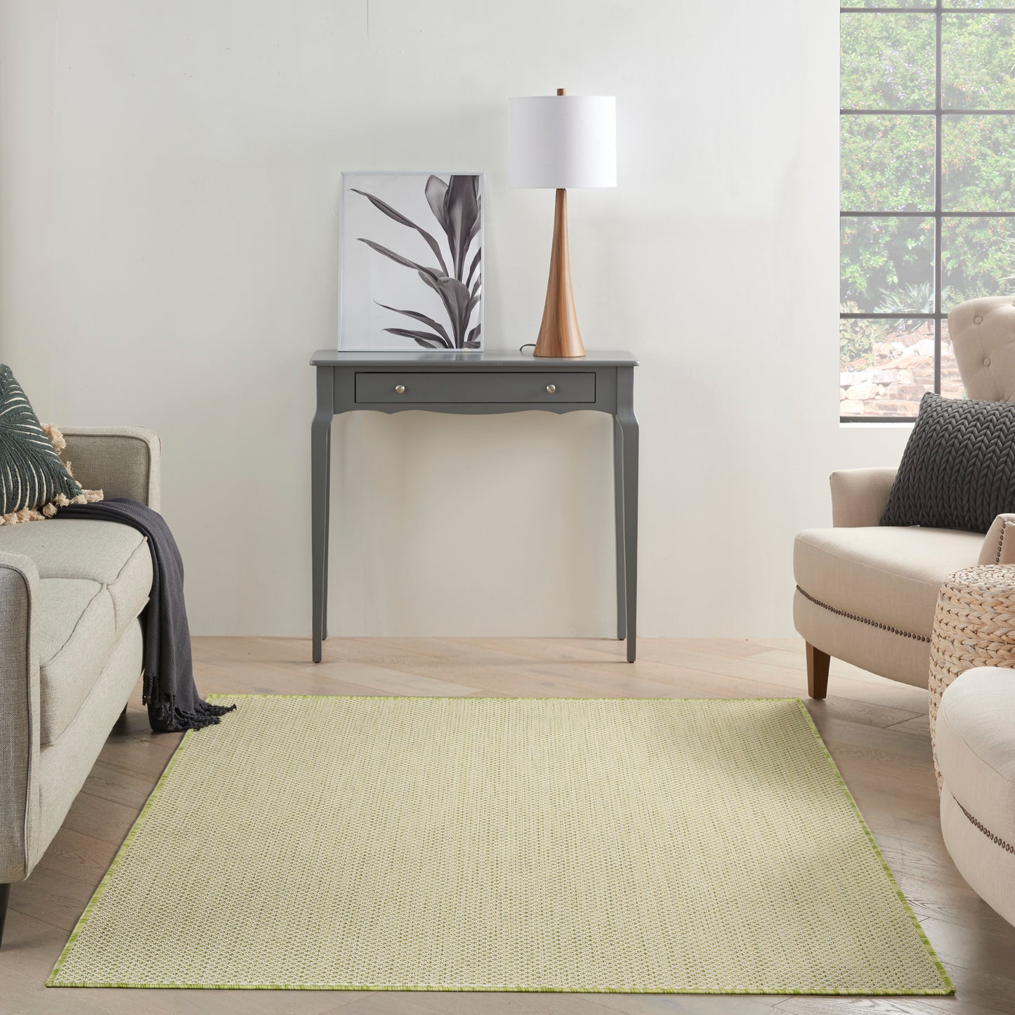 Light olive-green rectangular woven rug in a modern living room with gray console table, beige sofa and chair, and a white lamp.