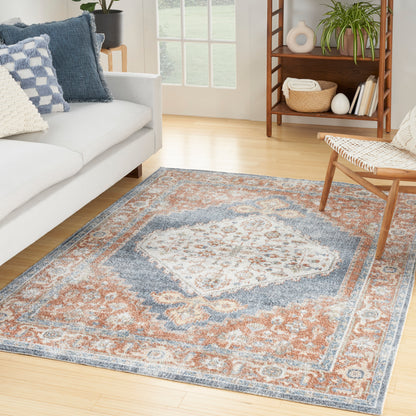 Soft-pile oriental area rug in blue, orange and ivory tones on a light-wood living room floor beside a gray sofa.