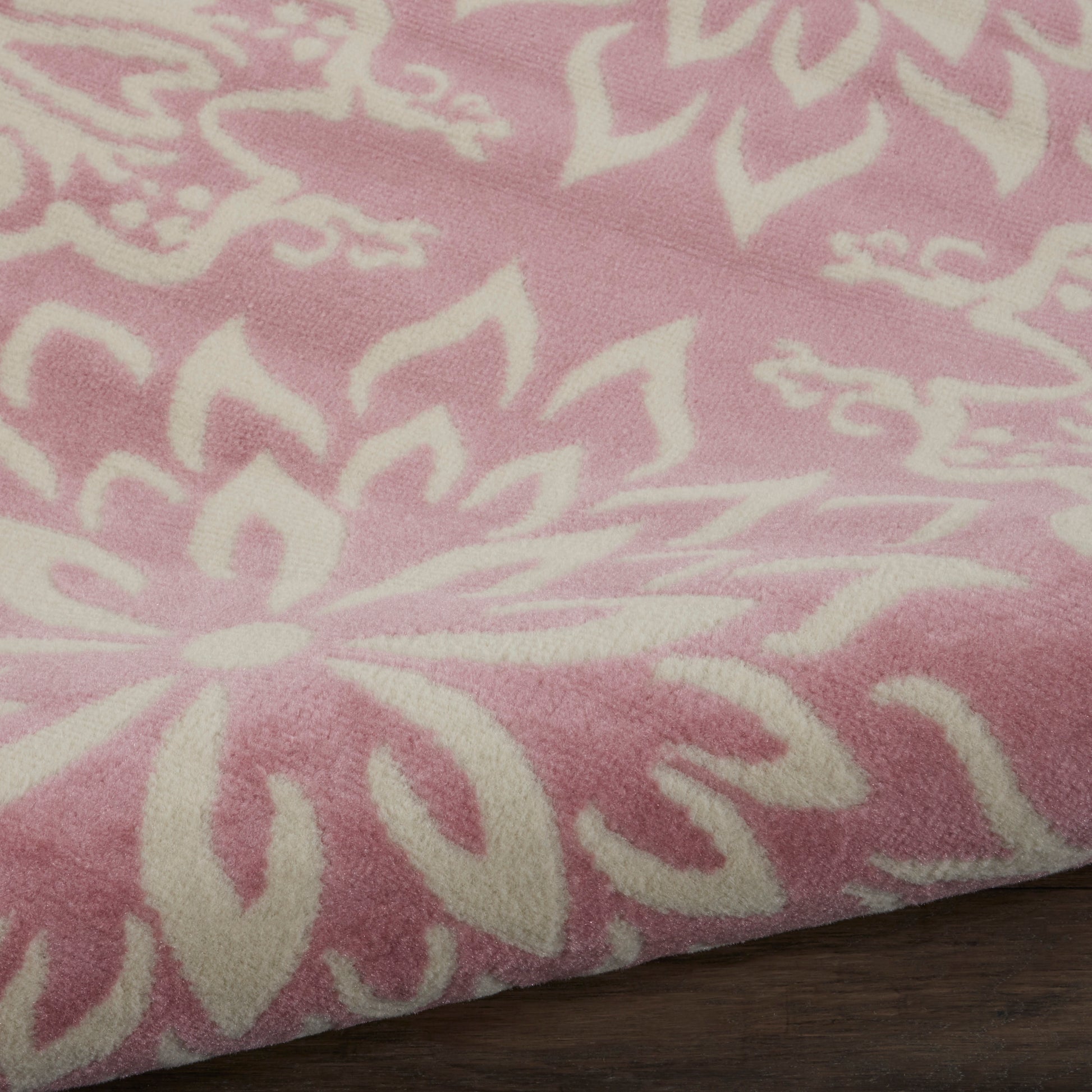 Pink rug with large white floral pattern, soft woven texture, decorative floor covering.