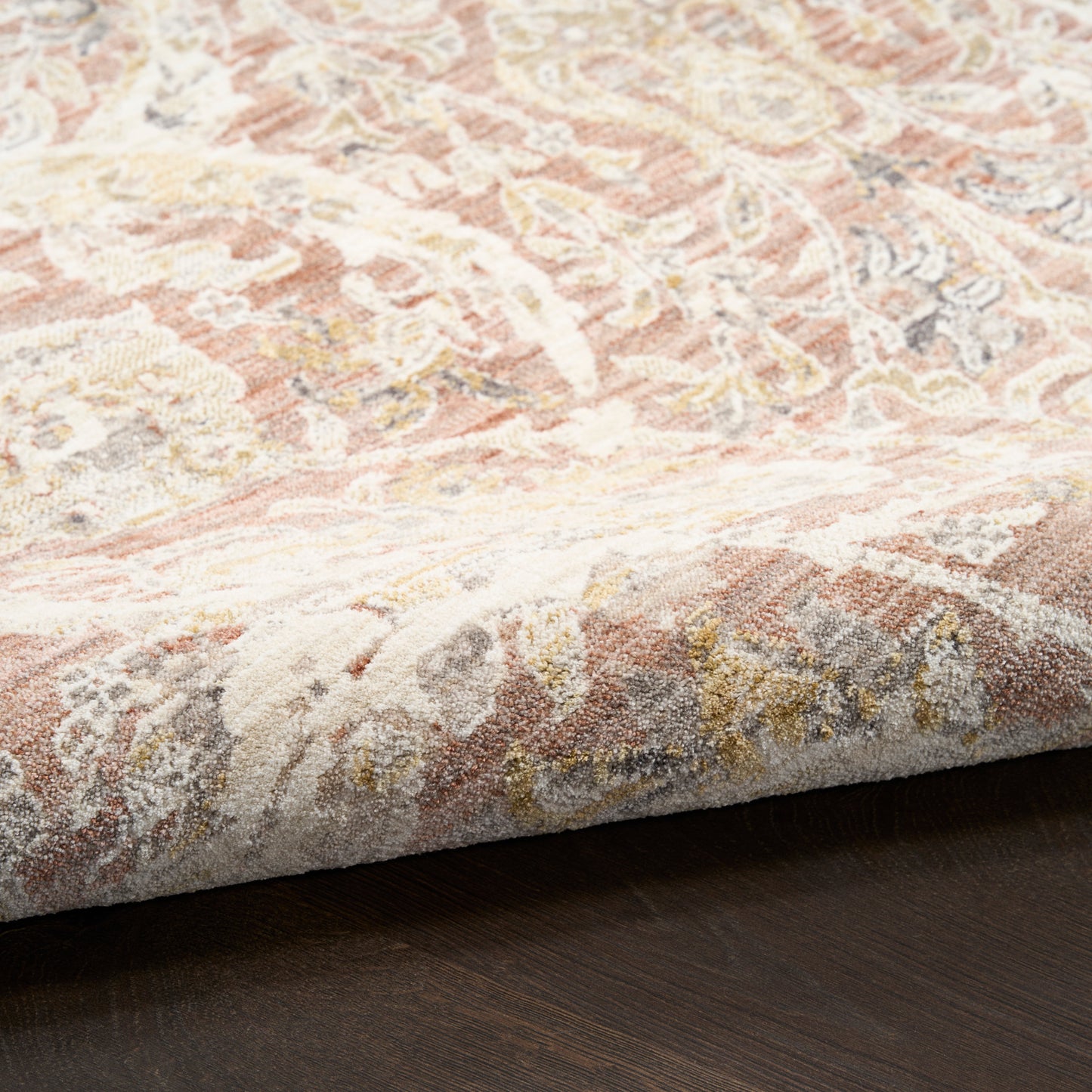 Close-up of pastel floral rug edge on dark wood floor; soft pinks, creams and beiges with a delicate pattern and gold accents.