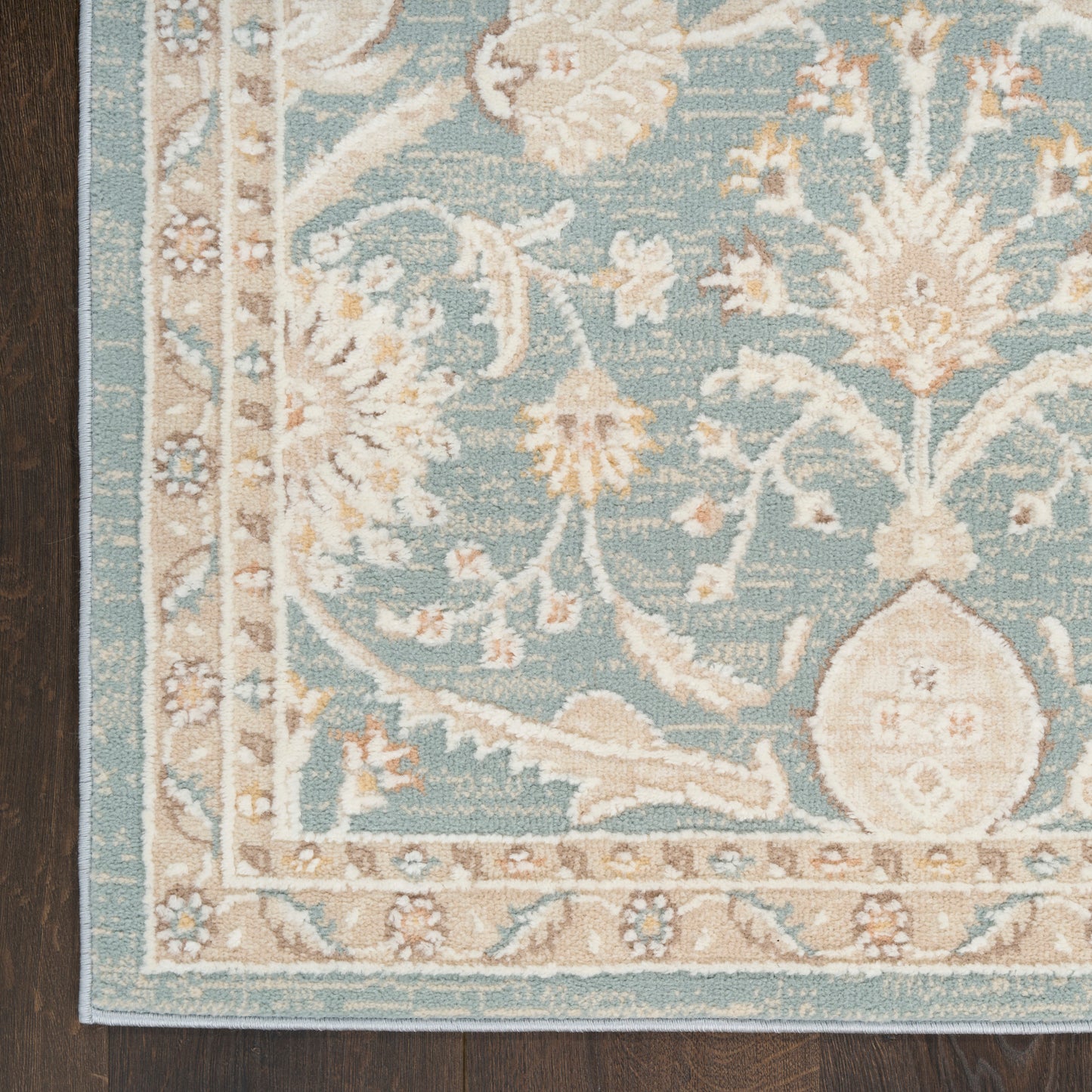 Teal oriental rug with ivory floral motifs and a beige decorative border on a dark wood floor.