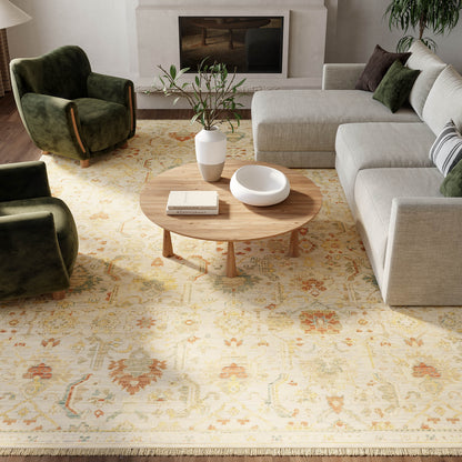 Cozy living room with a wooden coffee table on a beige patterned rug, gray sectional sofa, green velvet armchairs, and a fireplace.