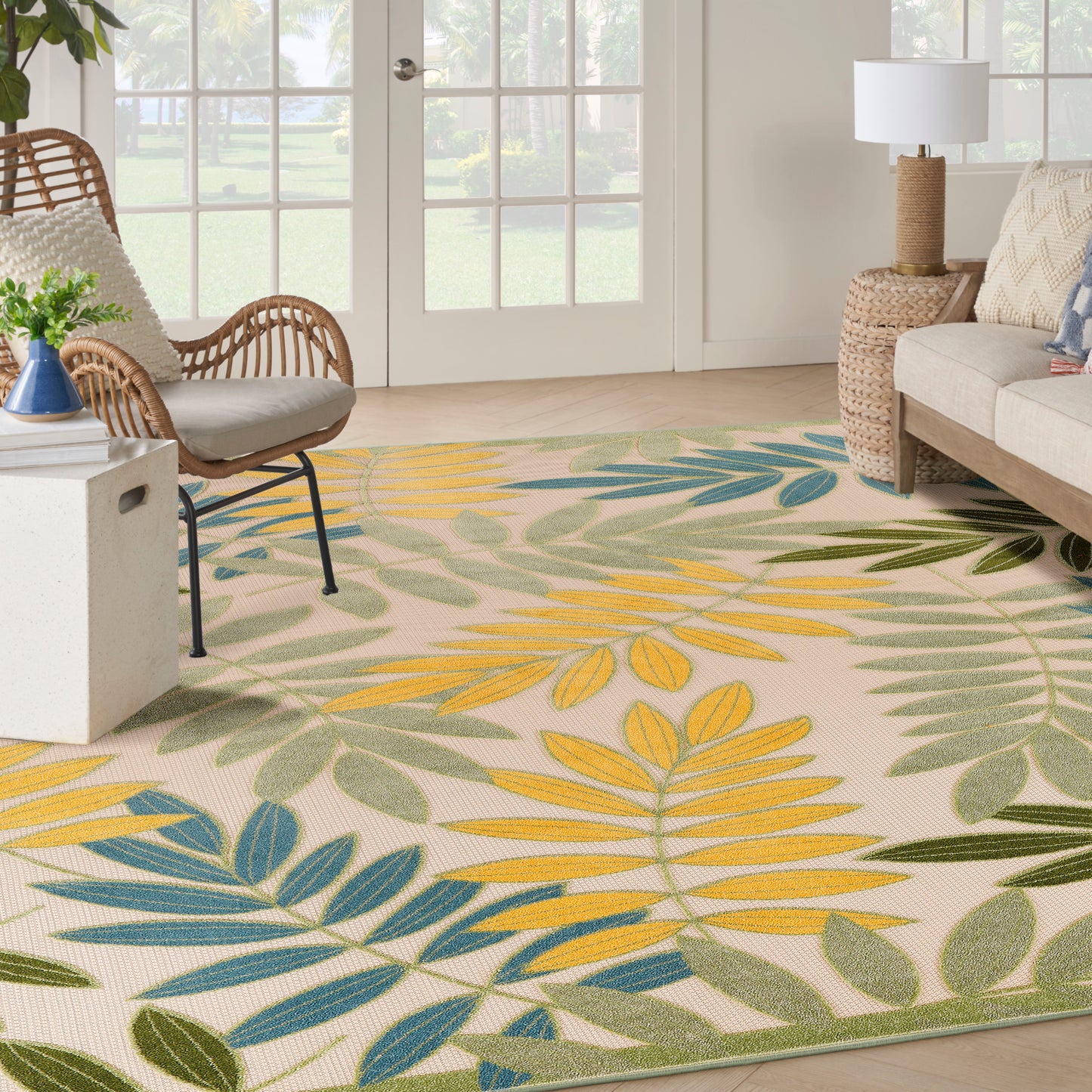Tropical leaf-print area rug in yellow, green and blue with a beige woven background, in a bright coastal living room.