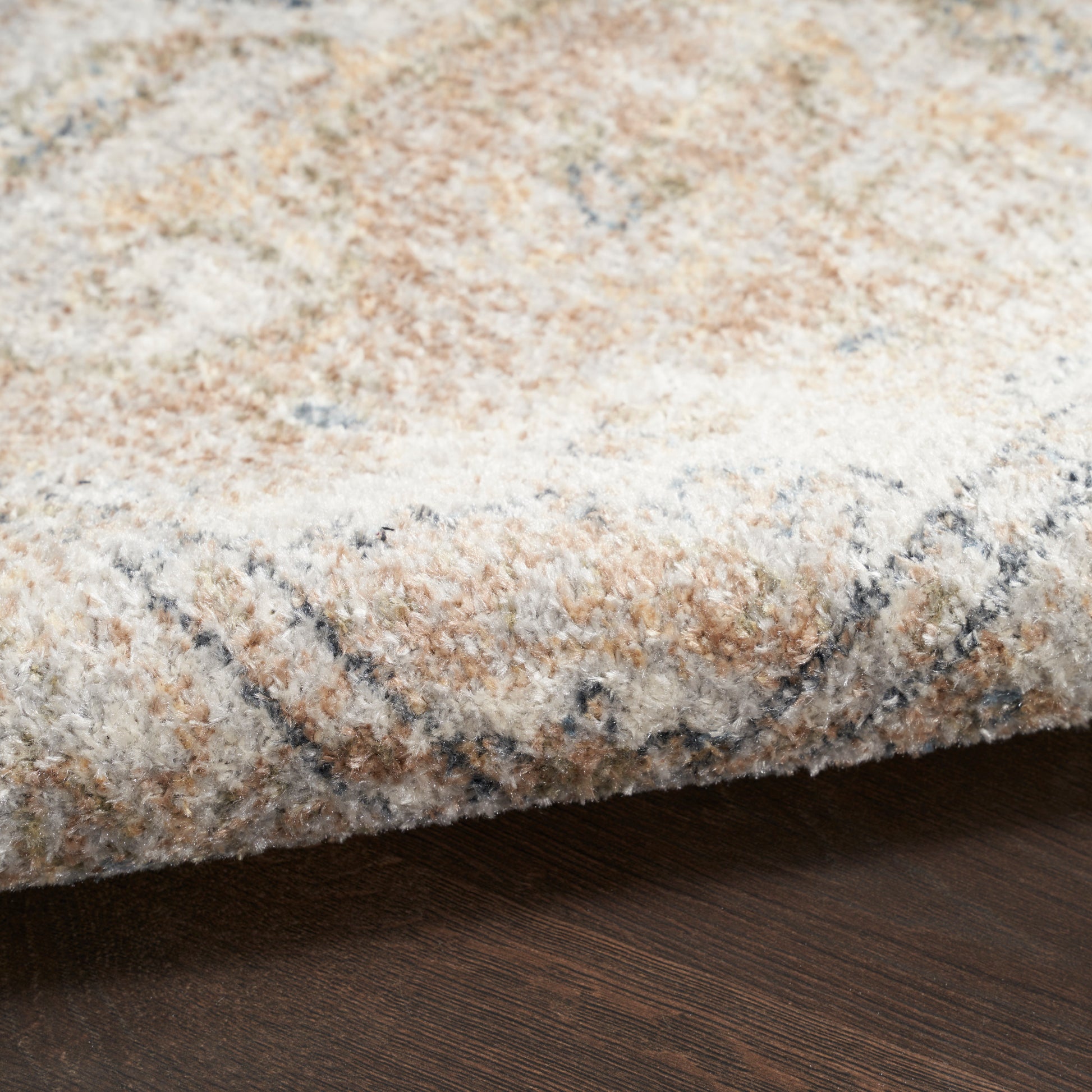 Soft beige, ivory and gray plush area rug with abstract pattern, folded edge resting on dark wood floor.