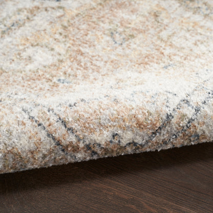 Soft beige, ivory and gray plush area rug with abstract pattern, folded edge resting on dark wood floor.