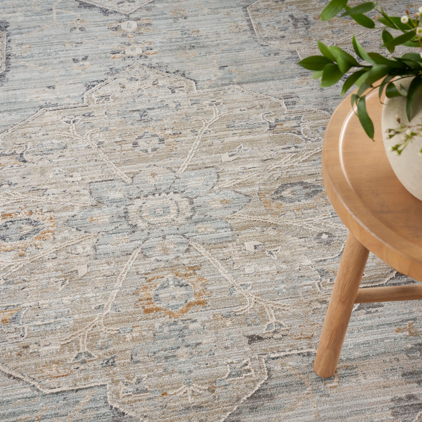 Blue-gray patterned rug with distressed floral motif; round wood table with a potted plant.