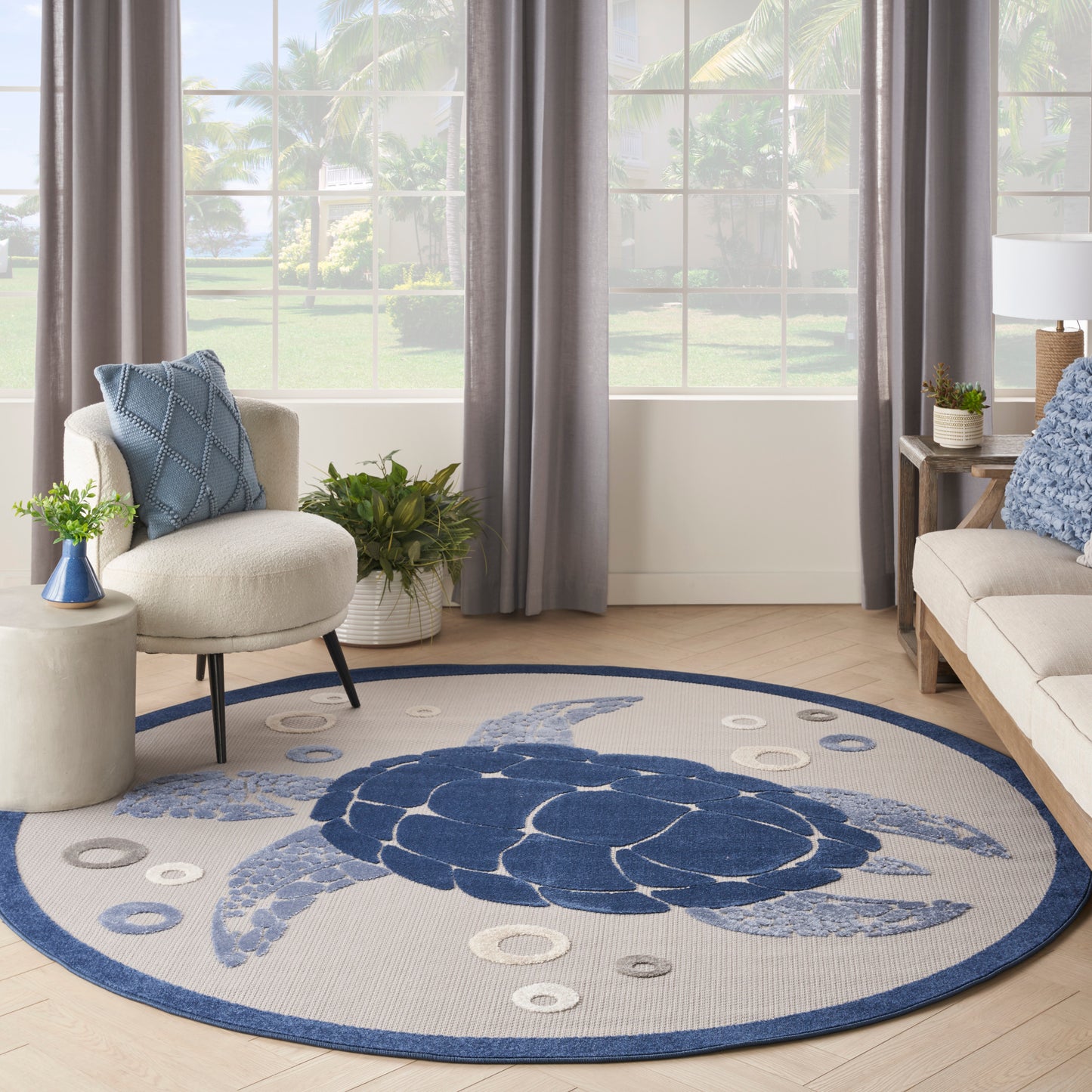 Round rug featuring a blue sea turtle on light gray, navy edge, in a beige living room with blue cushions & plants.
