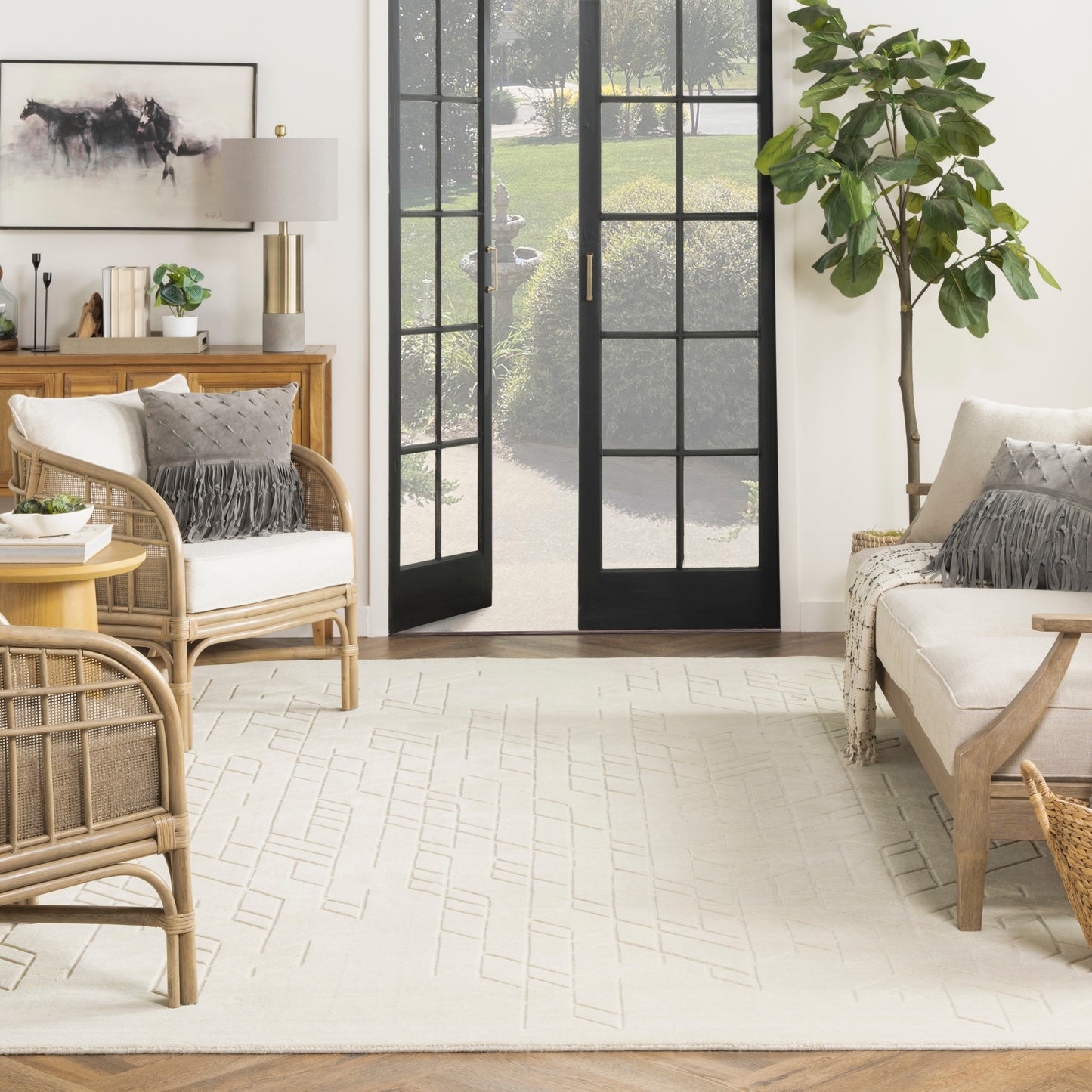 Bright living room with rattan furniture, neutral cushions, beige rug, and black-framed glass doors to outside.
