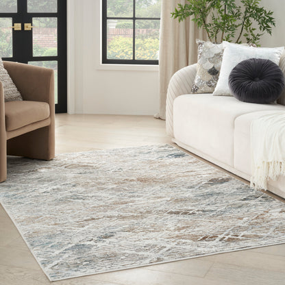 Light blue-gray abstract area rug in a modern living room with a white sofa, tan chair, and light wood floor.