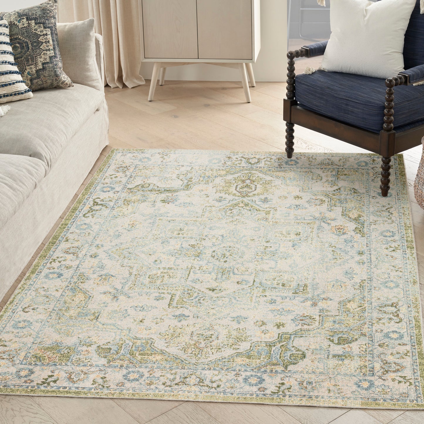 Soft blue & ivory oriental rug with pale green border in a living room beside a beige sofa & dark wood armchair.