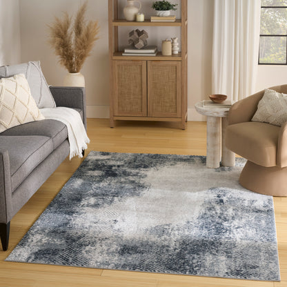 Cozy living room with a blue-gray abstract area rug (4' x 6'), gray fabric sofa, beige curved chair, and woven wood cabinet.