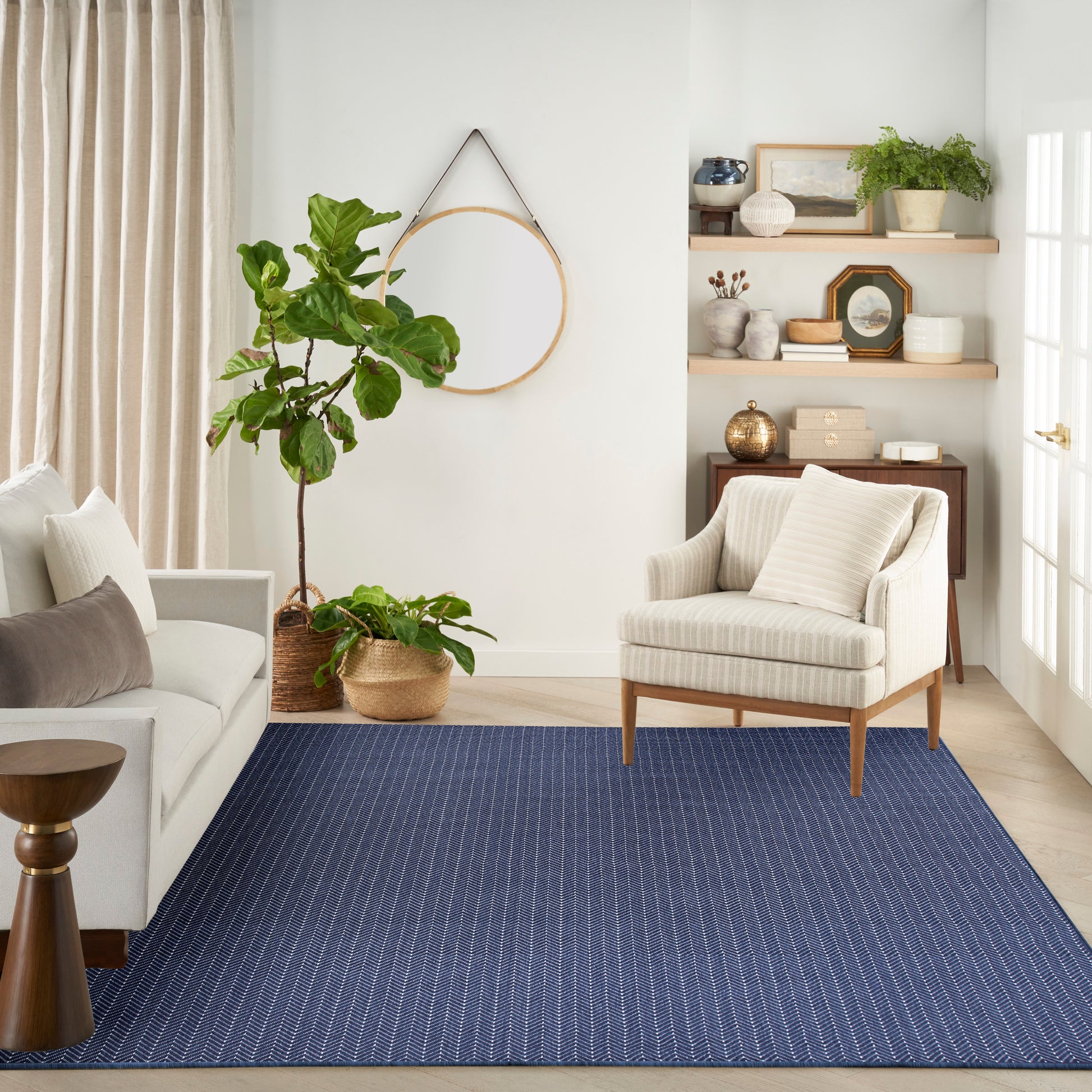 Cozy living room with navy striped area rug, beige armchair, gray sofa with cushions, and tall fiddle-leaf fig.