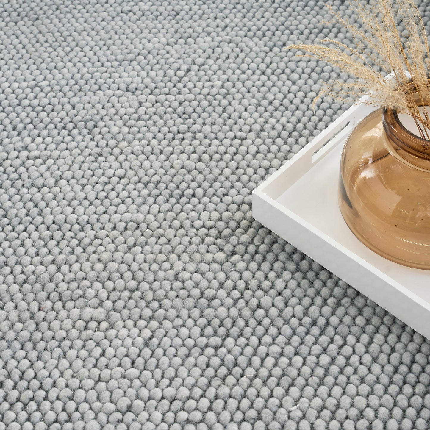 Light gray boucle rug with chunky tufted texture, white tray with amber glass vase & dried grasses.