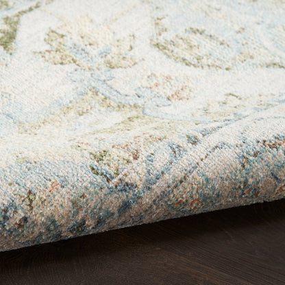 Pastel woven rug with cream base and blue, green, peach motifs; folded corner on dark wood floor.