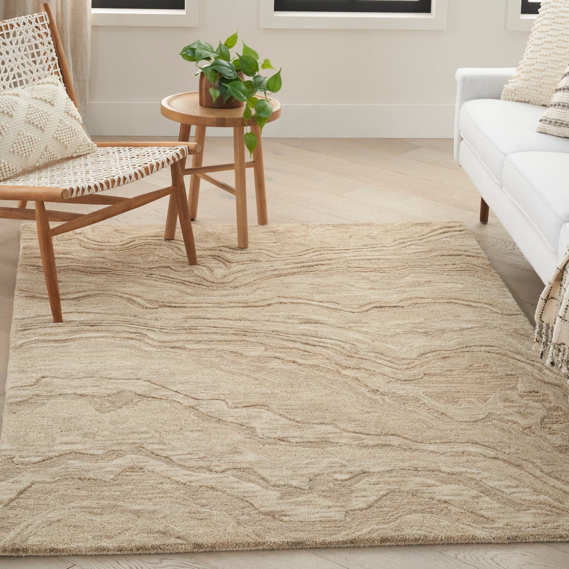 Beige wavy-textured area rug (5' x 7') in a bright living room with a mid-century wooden chair, round side table and plant.