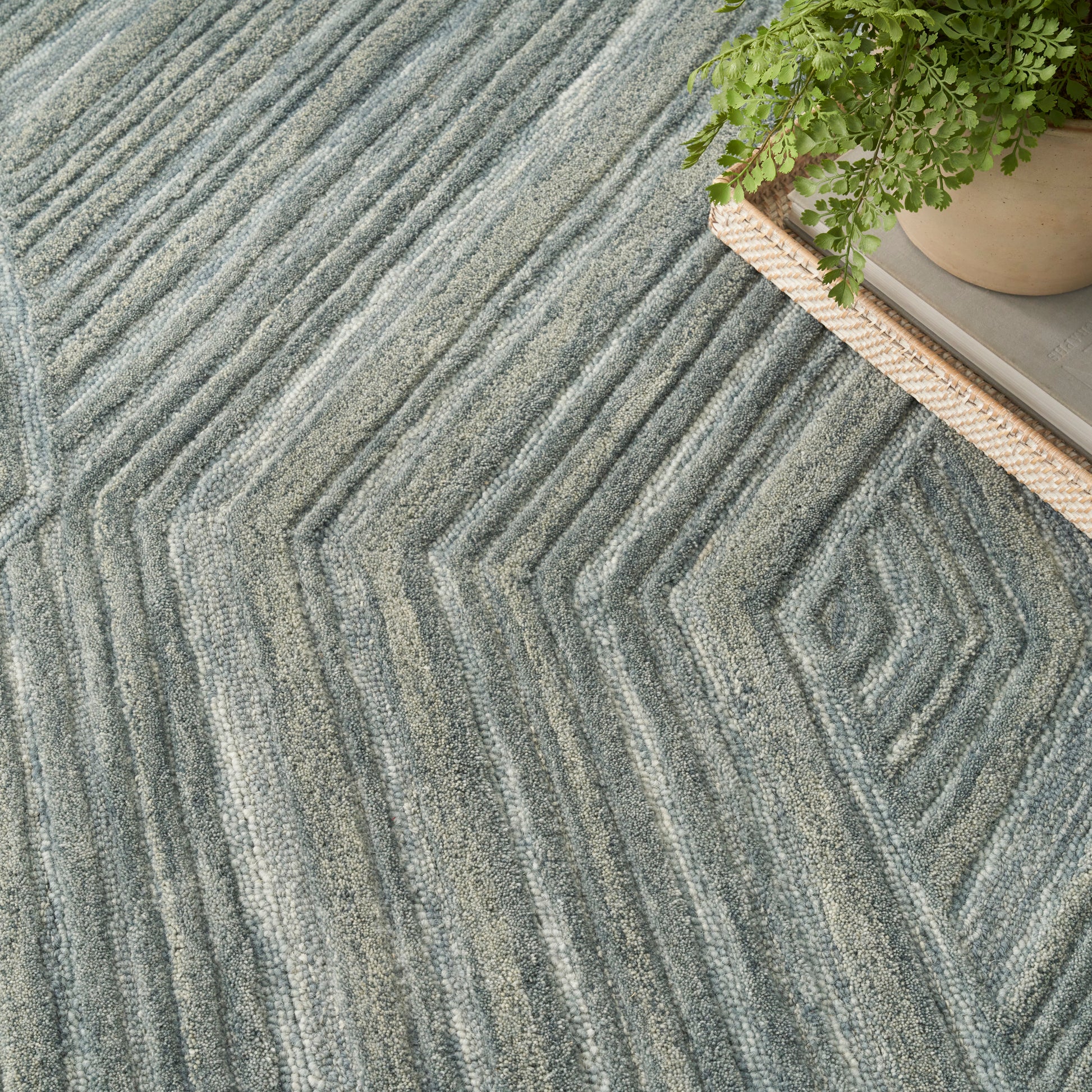 Gray zigzag textured rug with concentric chevron pattern and raised ridges; plant on a woven tray nearby.