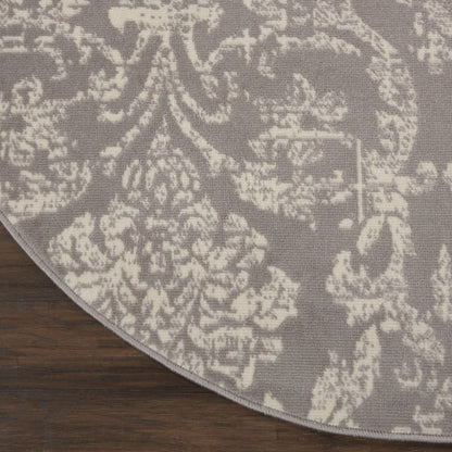 Round gray rug with white damask floral pattern on dark wood floor.