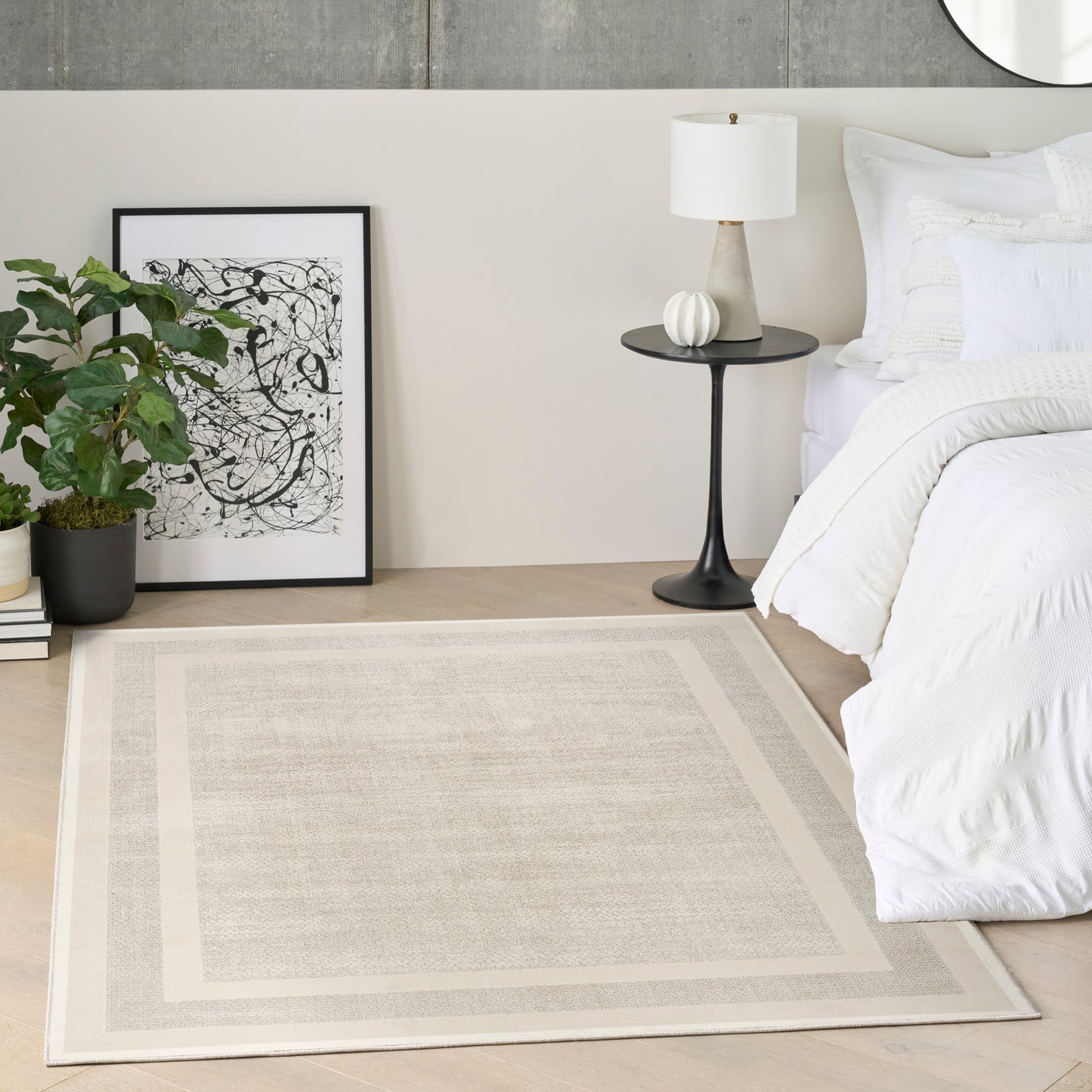 Neutral modern bedroom with beige rug, white bedding, black round nightstand, white lamp, framed abstract art, potted plant.