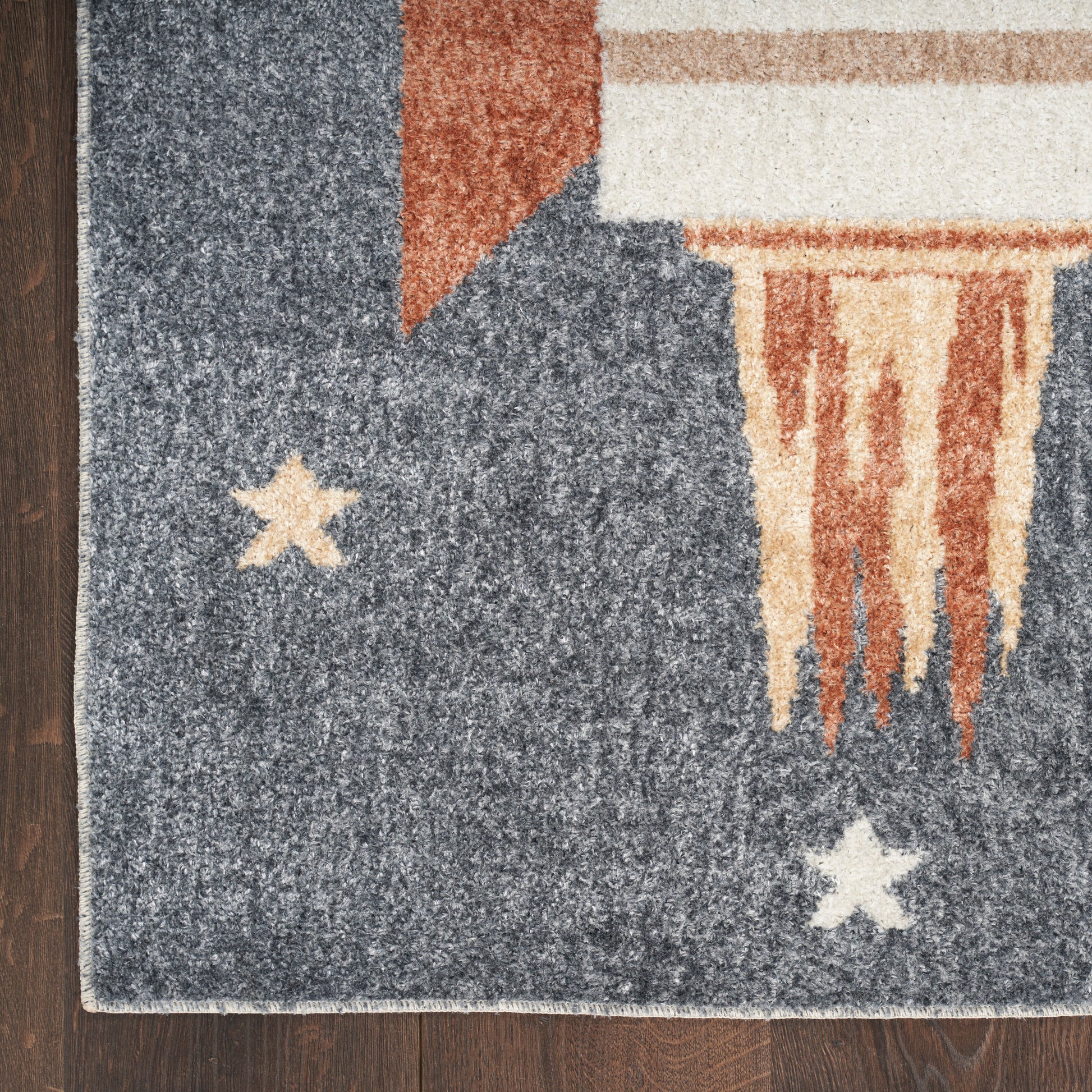 Textured navy area rug with cream stars, beige fringe and tan accents on dark wood floor.