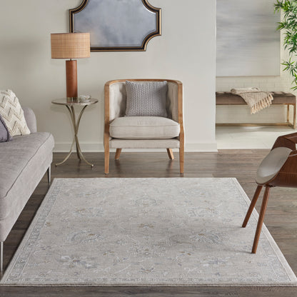 Neutral living room with gray fabric sofa, cream wood-frame chair, glass side table, wooden lamp, pale patterned rug.