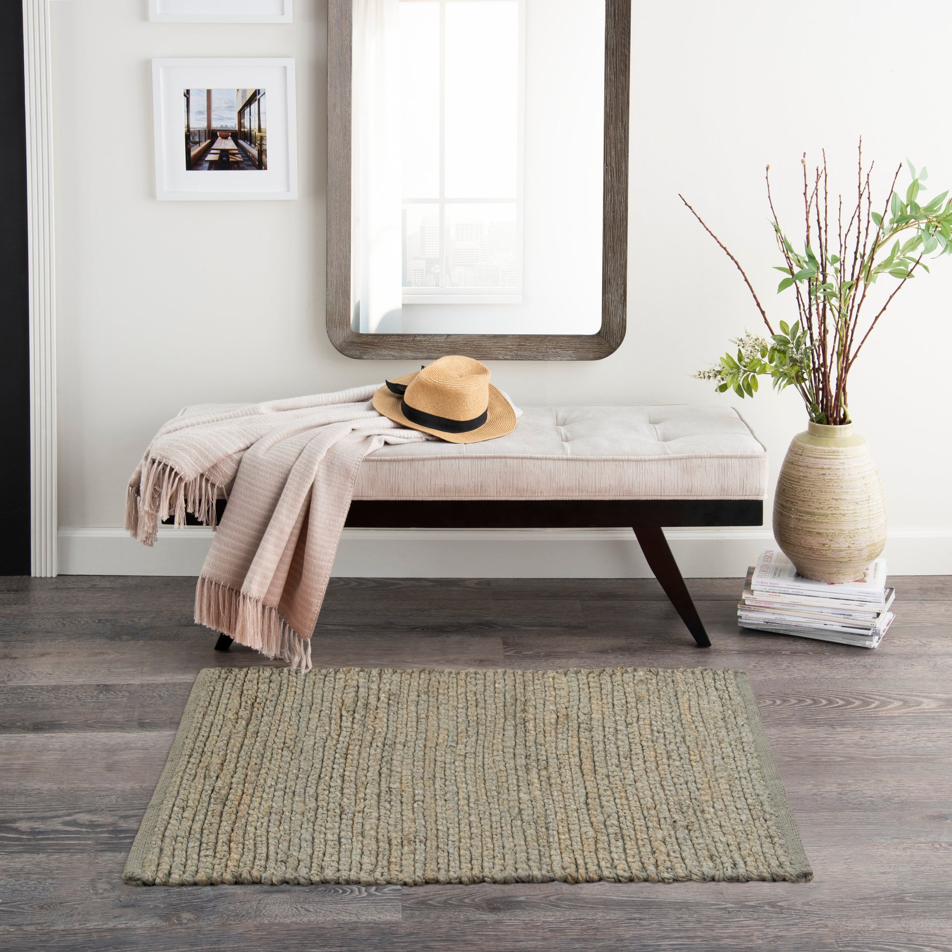 Cream tufted bench with dark wood legs, beige throw, straw hat, in front of a wooden-framed mirror; vase with branches.