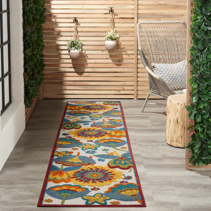Long floral runner rug in orange, teal & yellow on a wooden deck; outdoor seating with wicker chair and hanging planters.