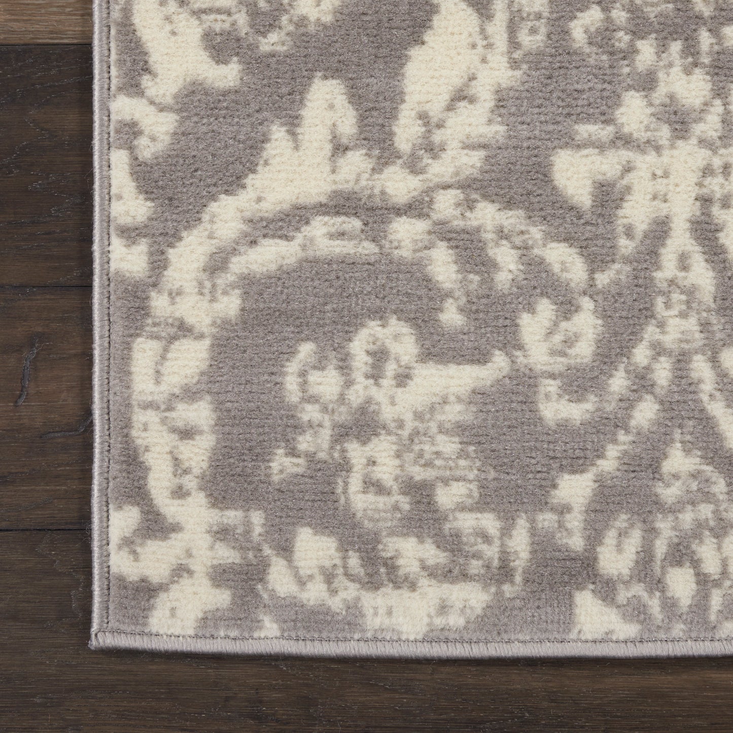 Gray & ivory damask rug with floral pattern, flatwoven look, light gray binding edge on hardwood floor.
