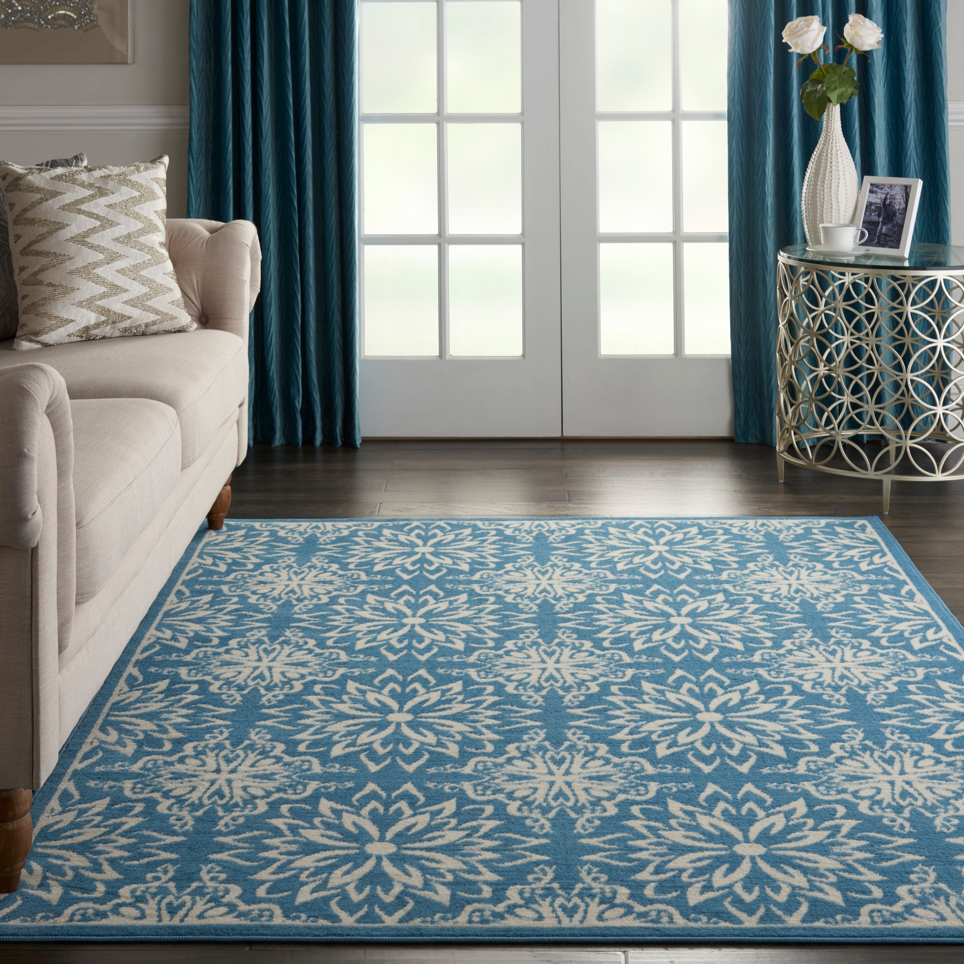Blue and white floral area rug in a living room with a beige sofa, teal curtains, and a decorative side table.