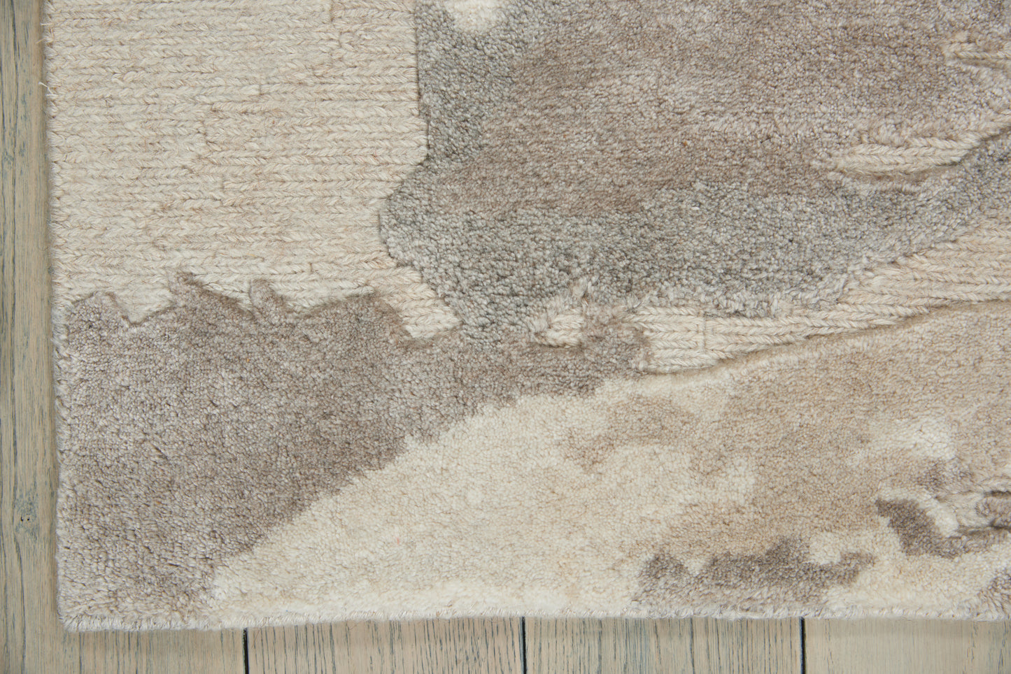 Beige and taupe shag area rug with abstract pattern on a light wood floor.