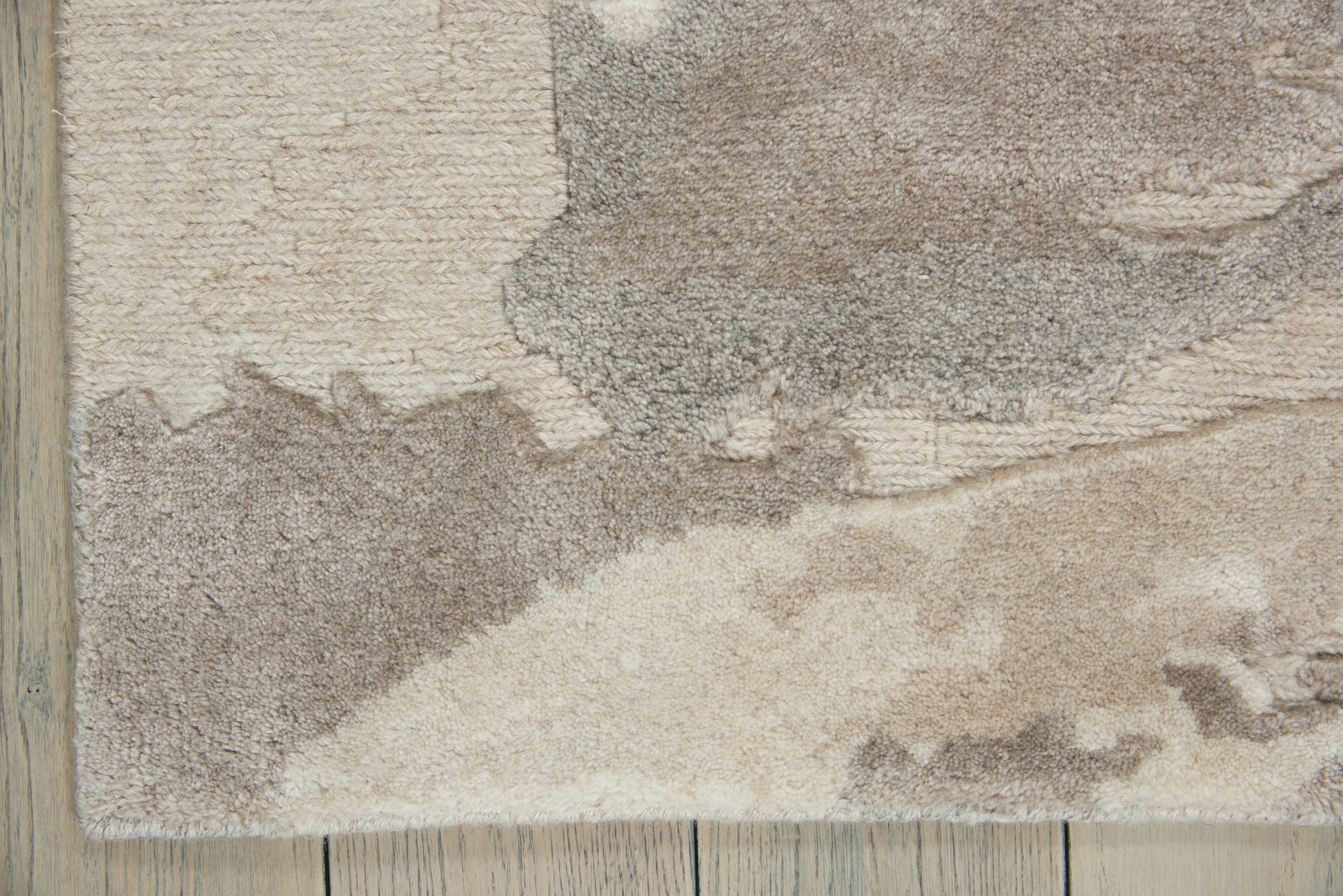 Beige and taupe shag area rug with abstract pattern on a light wood floor.