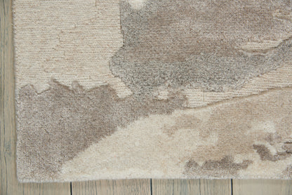 Beige and taupe shag area rug with abstract pattern on a light wood floor.
