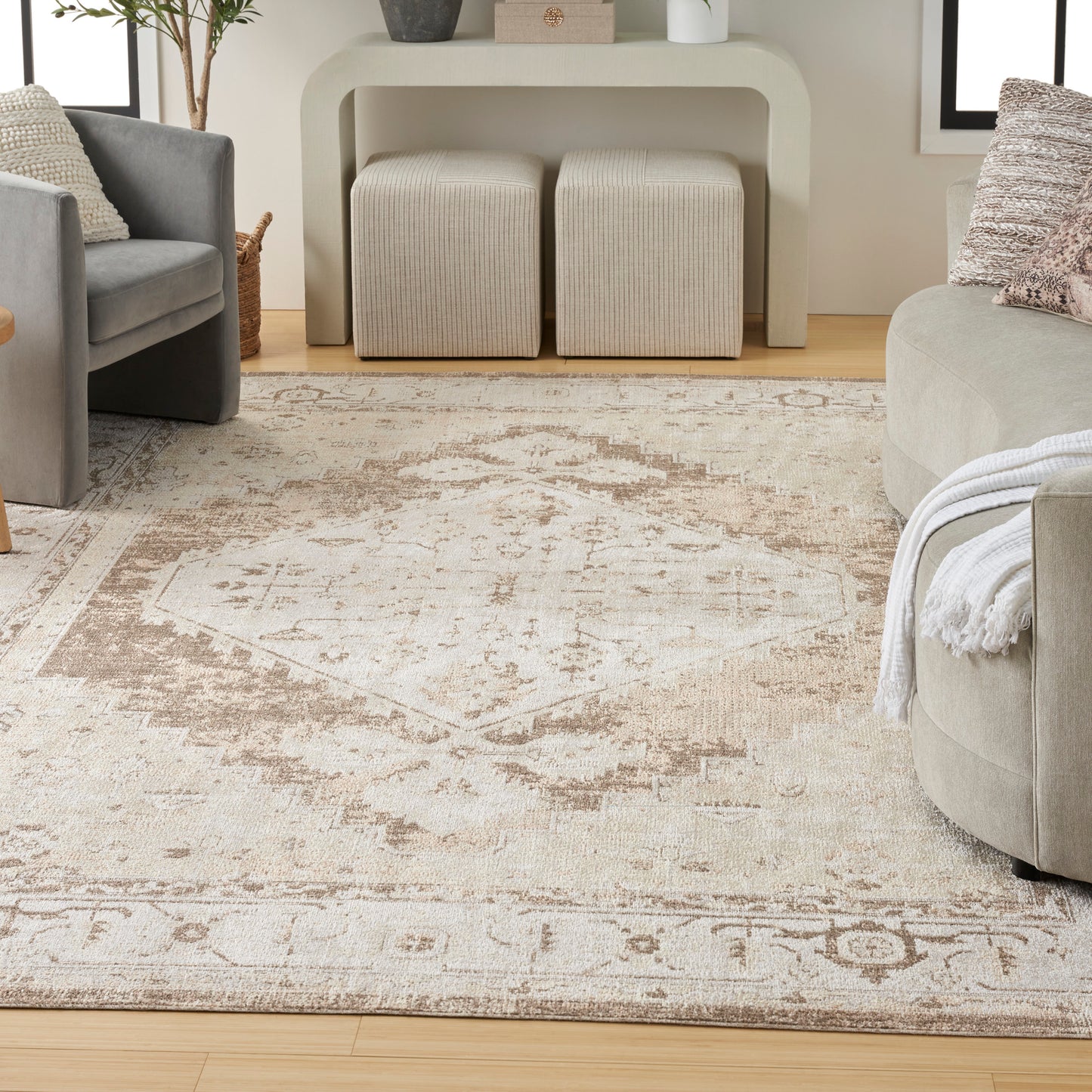 Beige vintage-style area rug with faded oriental motif, plush texture, in a modern gray living room with sofa and ottomans.