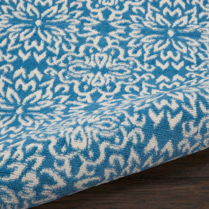 Blue & white ikat-style rug runner with geometric motif, folded edge on dark wood floor.