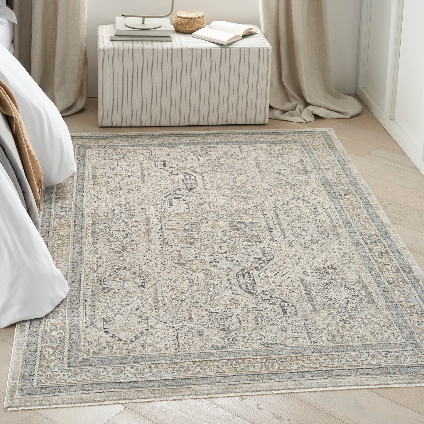 Beige-gray distressed Persian-style area rug on light wood floor in a bedroom with a striped ottoman.