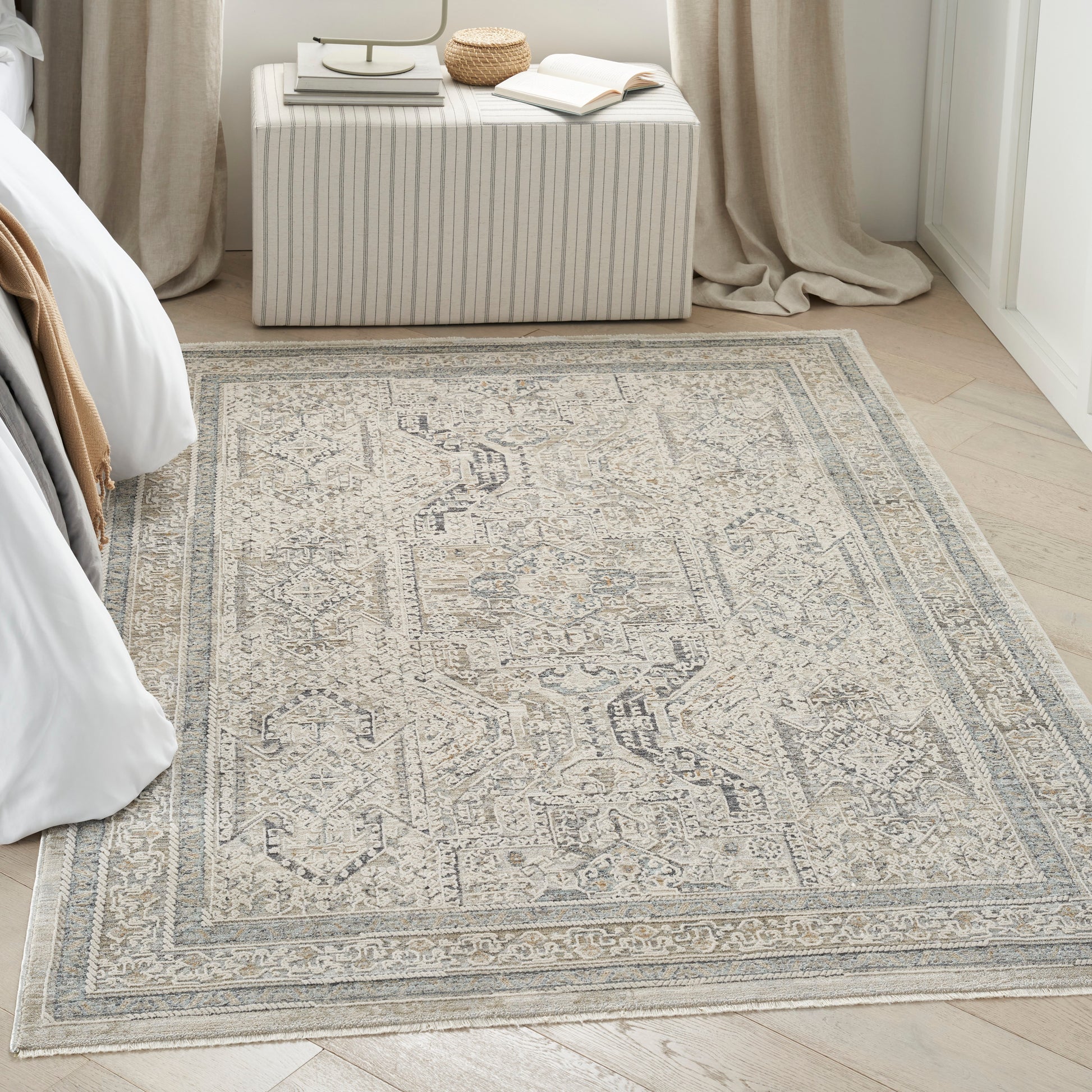 Beige-gray distressed Persian-style area rug on light wood floor in a bedroom with a striped ottoman.