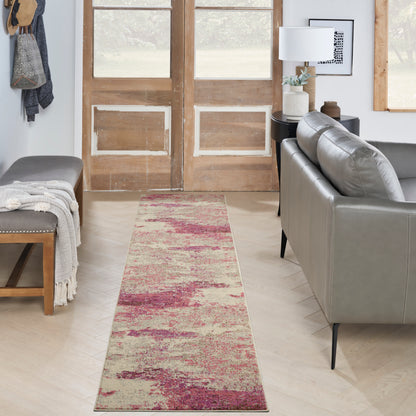 Long pink-red beige abstract rug runner on light wood floor with gray sofa, wooden double doors, and bench.