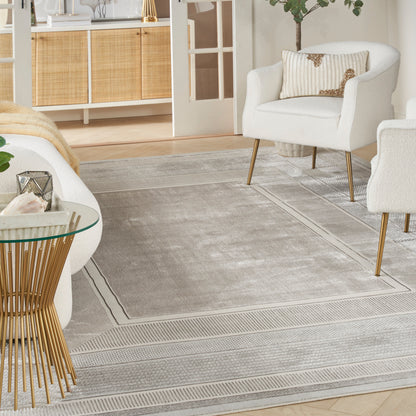 Light gray bordered area rug in a modern living room with white chairs on gold legs and a round glass-top side table.