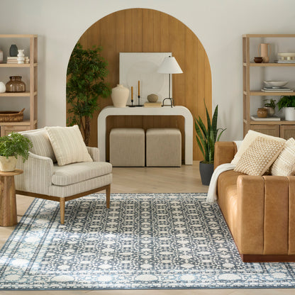 Blue patterned rug in a living room, 8' x 10', on a wooden floor, with a tan leather sofa, cream armchairs, and a wooden arch wall with a console table.