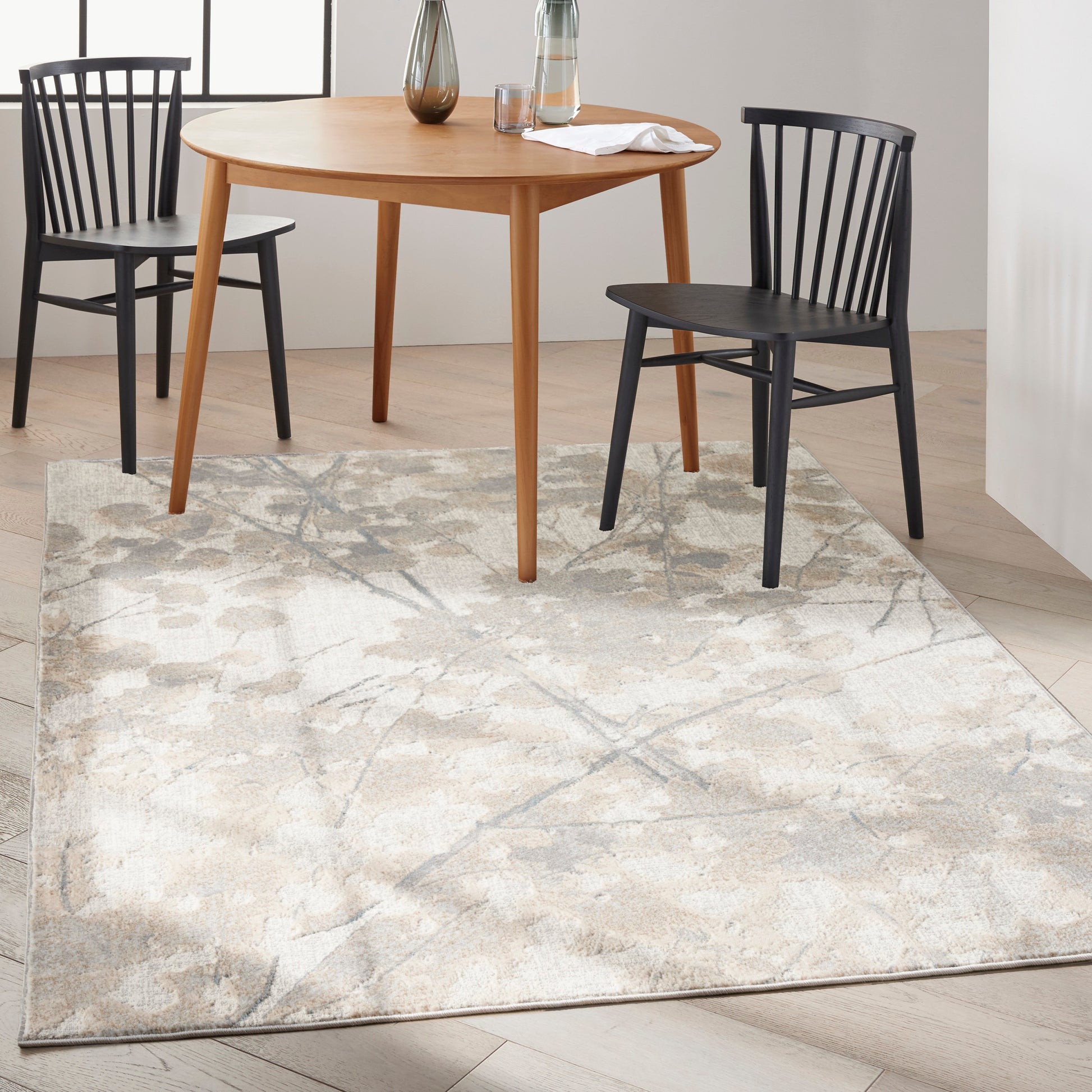 Beige abstract-pattern area rug under a round light-wood dining table with black spindle chairs; modern dining room scene.