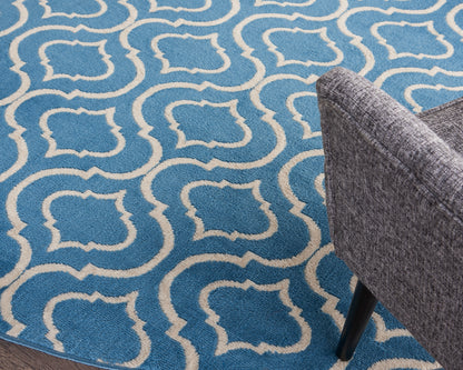 Blue rug with white interlocking geometric trellis pattern; grey upholstered chair leg visible on the right.