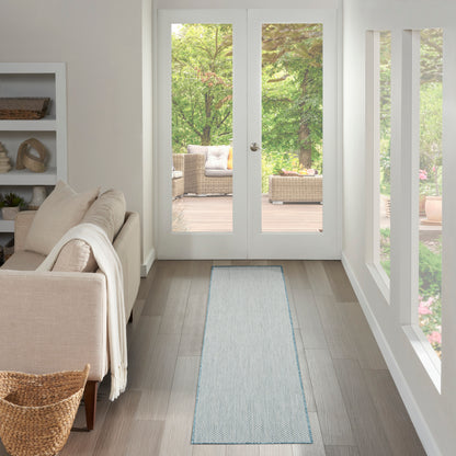 Bright living room with beige sofa, white shelves, light wood floor, blue-gray runner rug, and glass French doors to garden.