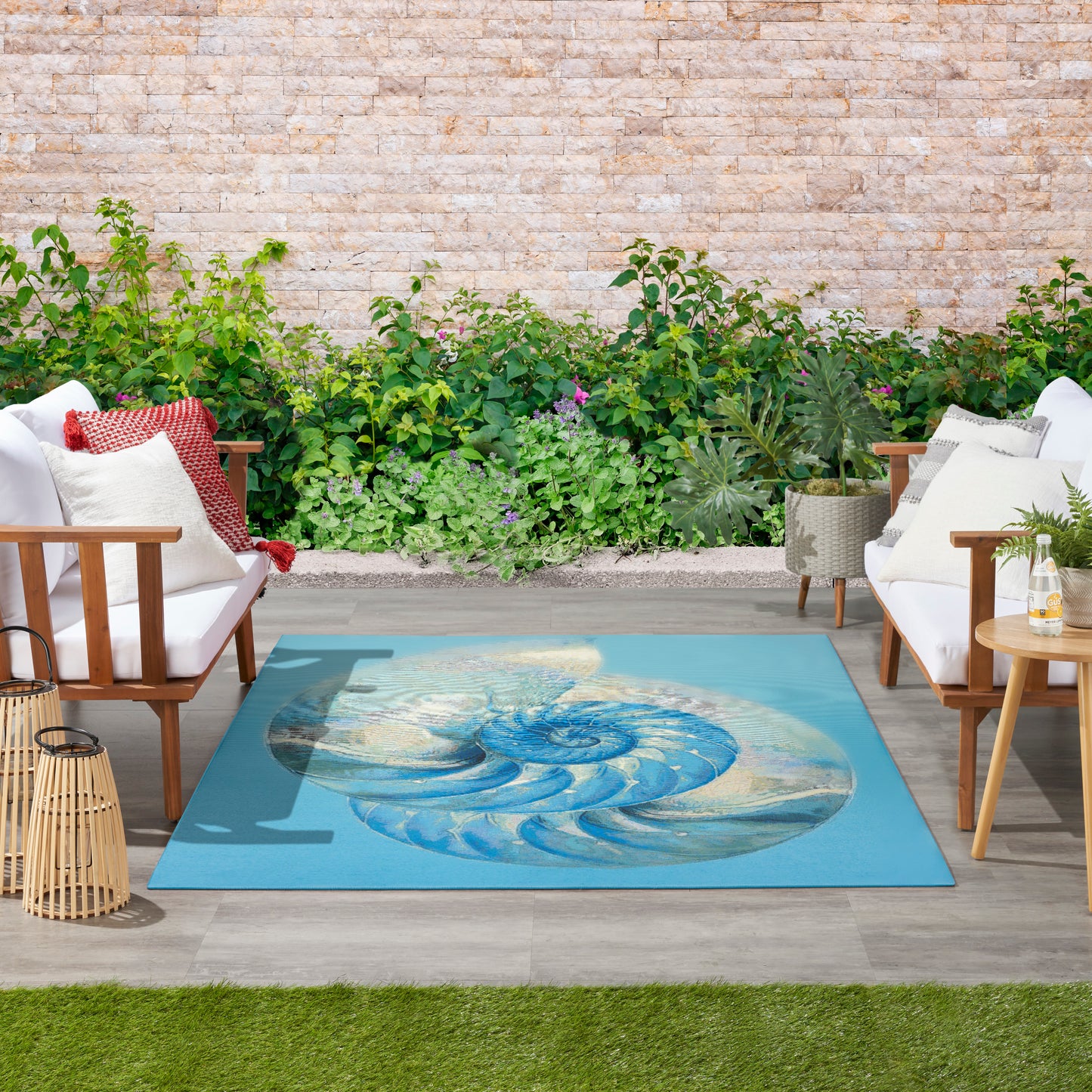 Outdoor seating area with white cushioned wooden chairs around a teal rug featuring a blue spiral shell, garden backdrop.