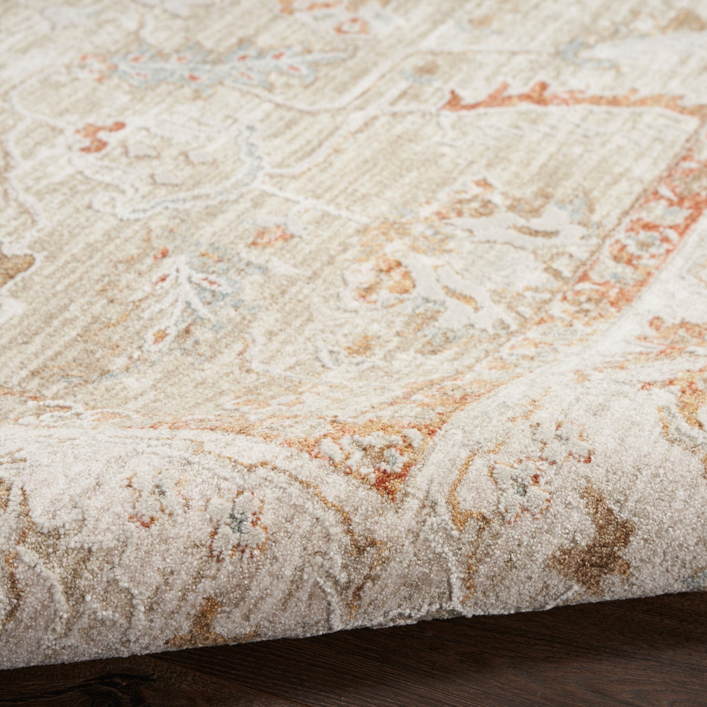 Beige cream oriental rug with subtle orange accents and intricate floral pattern; close-up edge on dark wooden floor