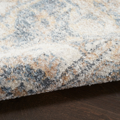Close-up of a plush area rug in blue, gray, ivory and beige tones with a soft shaggy pile on dark wood floor.